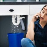 A person on the phone sitting in front of a leaking pipe in her kitchen